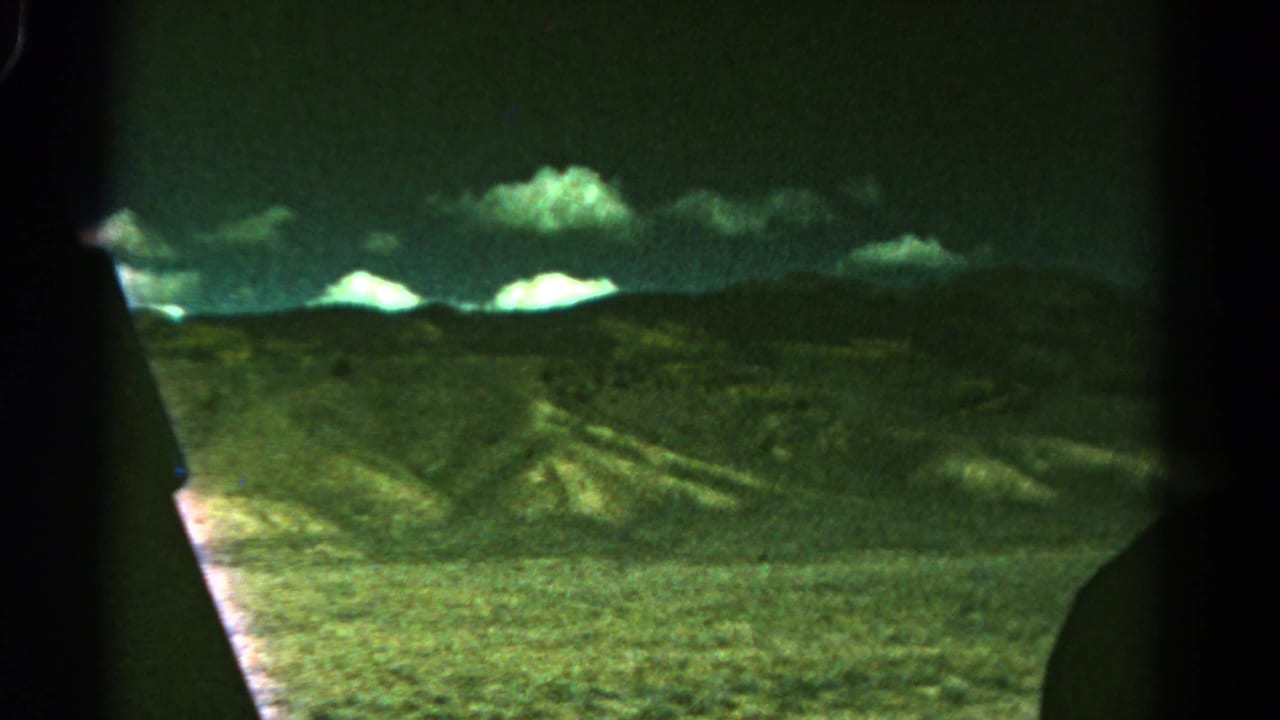 1967 Colorado 8mm frame showing distant mountain ridges and dry rolling hills from inside a moving car.