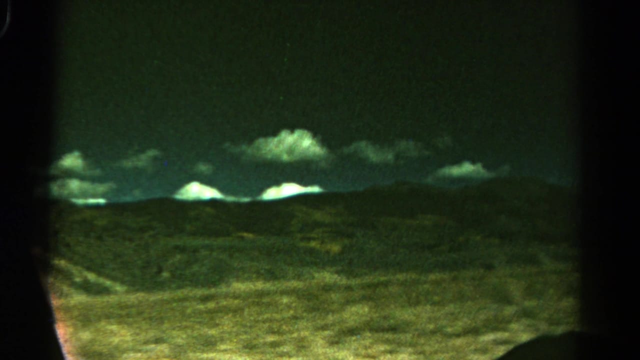 Mountain ridges and low hills framed by dark vertical car-window shapes.