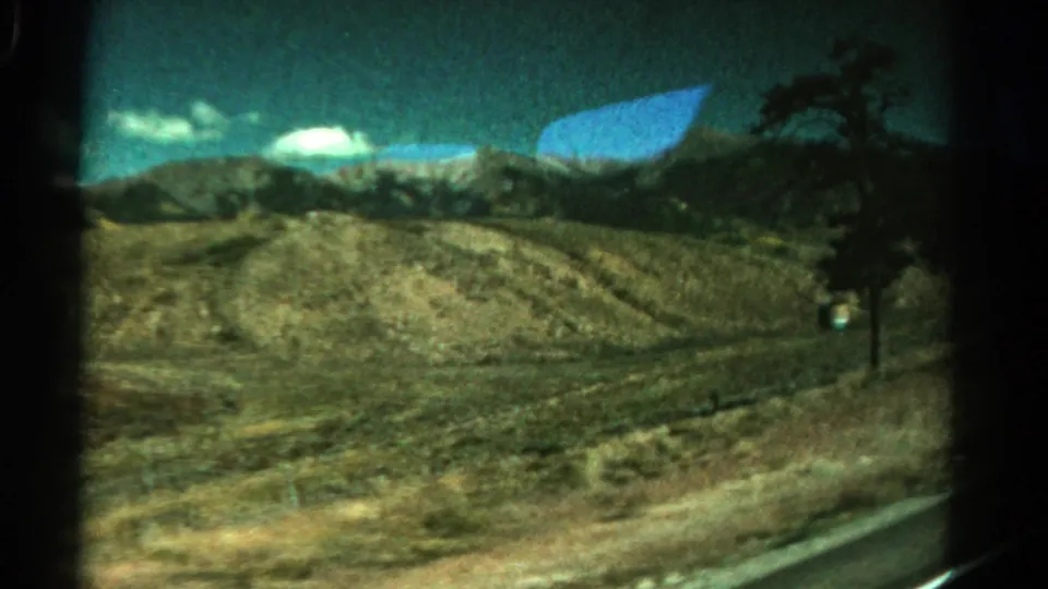 Passenger-side 8mm view of Colorado hills with a roadside edge, distant clouds, and a dark tree silhouette.