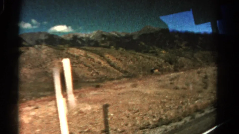 1967 Colorado home-movie view through a car window, showing rocky hills, distant mountains, scrub land, and a roadside pole.