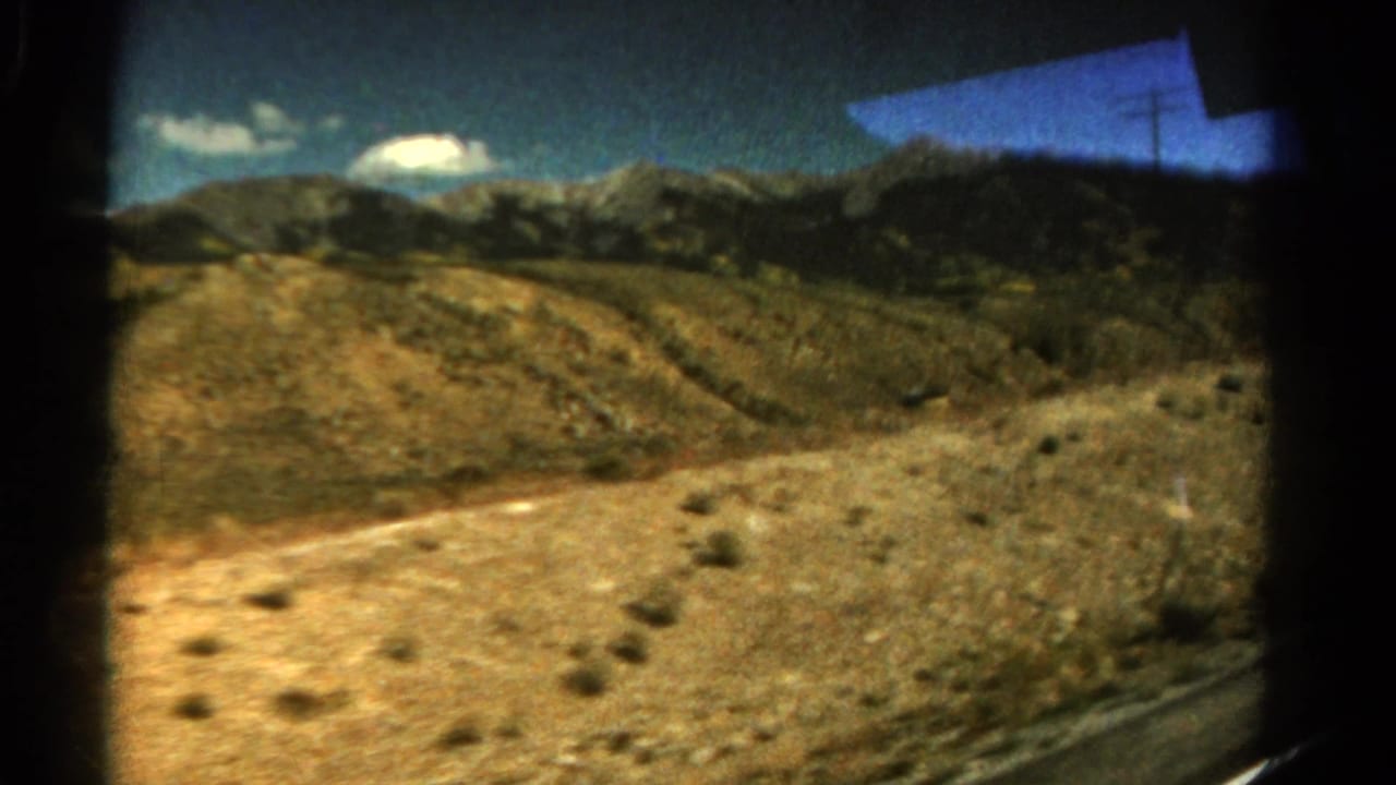 Sunlit rocky slope and mountain ridge passing outside a vehicle window.