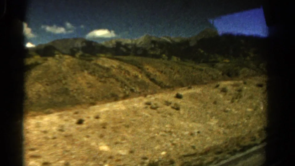 A 1967 Colorado road-trip frame shows scrubby hills, distant mountains, bright clouds, and dark interior window framing.
