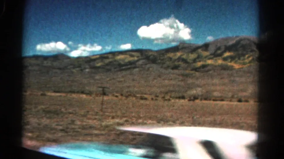 1967 Colorado 8mm car-window view across dry open land toward mountains, with a bright vehicle edge entering the lower frame.