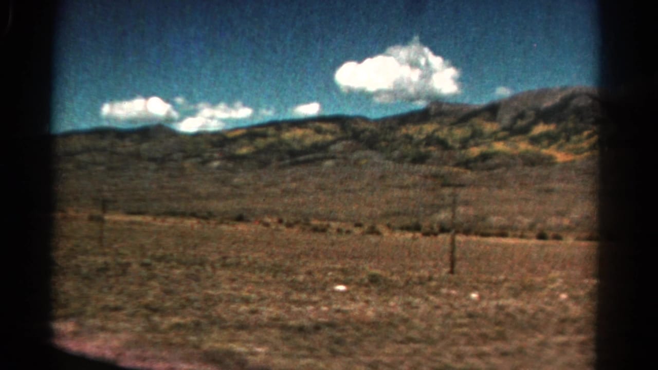 Dry open countryside with low hills, utility poles, blue sky, and white clouds.