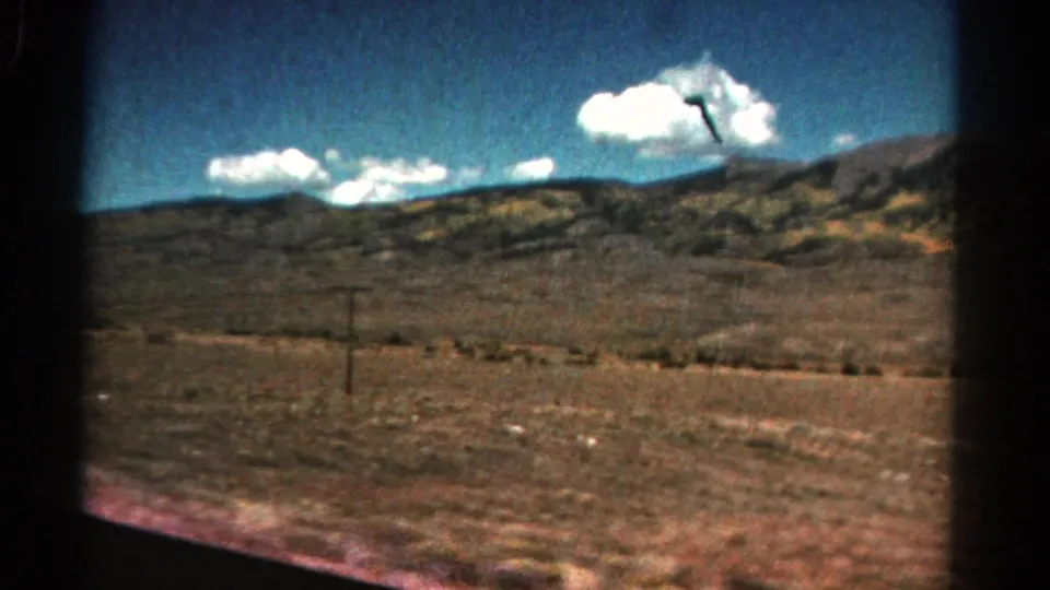 1967 Colorado 8mm frame with motion-softened dry countryside, low hills, utility pole, and clouded blue sky.