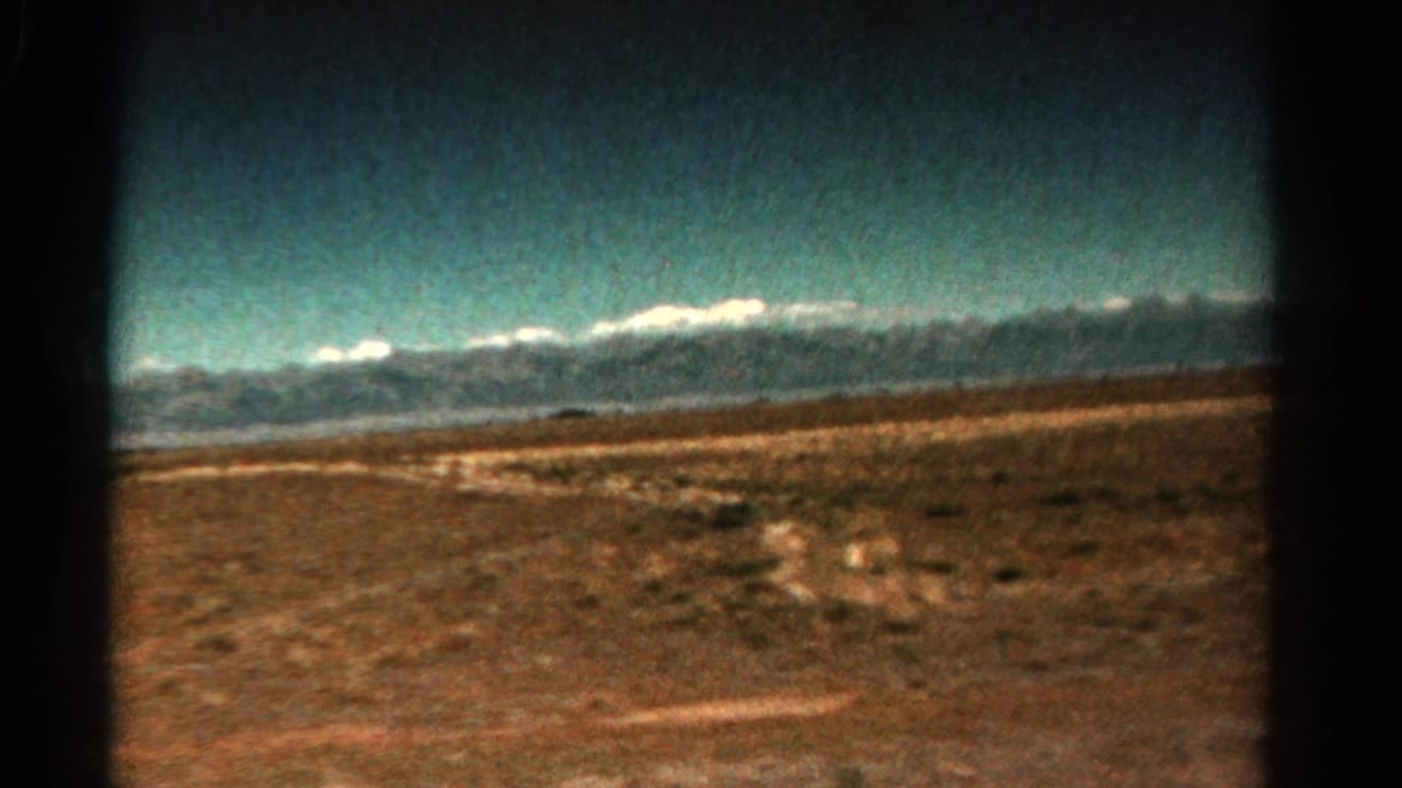 Open scrubland and faint track leading toward distant mountains beneath a bright sky.