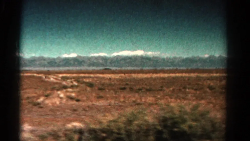 1967 Colorado 8mm view of dry brush and pale ground tracks with snow-touched mountains in the distance.