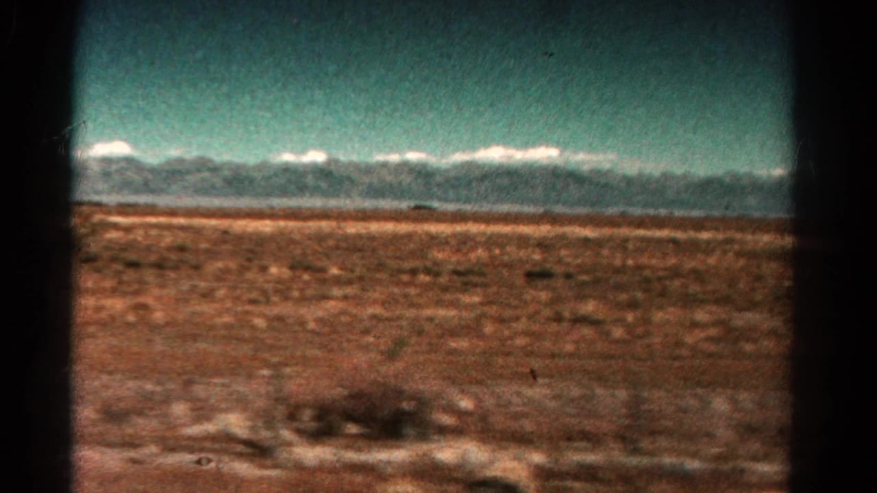 Distant snow-capped mountains beyond reddish scrubland, seen through dark film-frame borders.