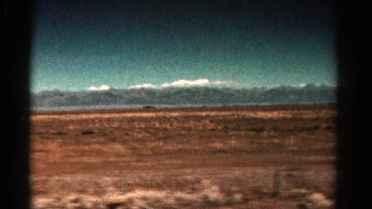 1967 Colorado travel footage frame with a broad scrub plain and snow-bright mountain peaks along the horizon.