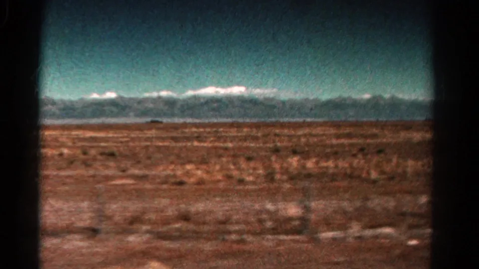 1967 Colorado 8mm travel frame showing snow-capped peaks along the horizon and motion-blurred arid terrain in the foreground.