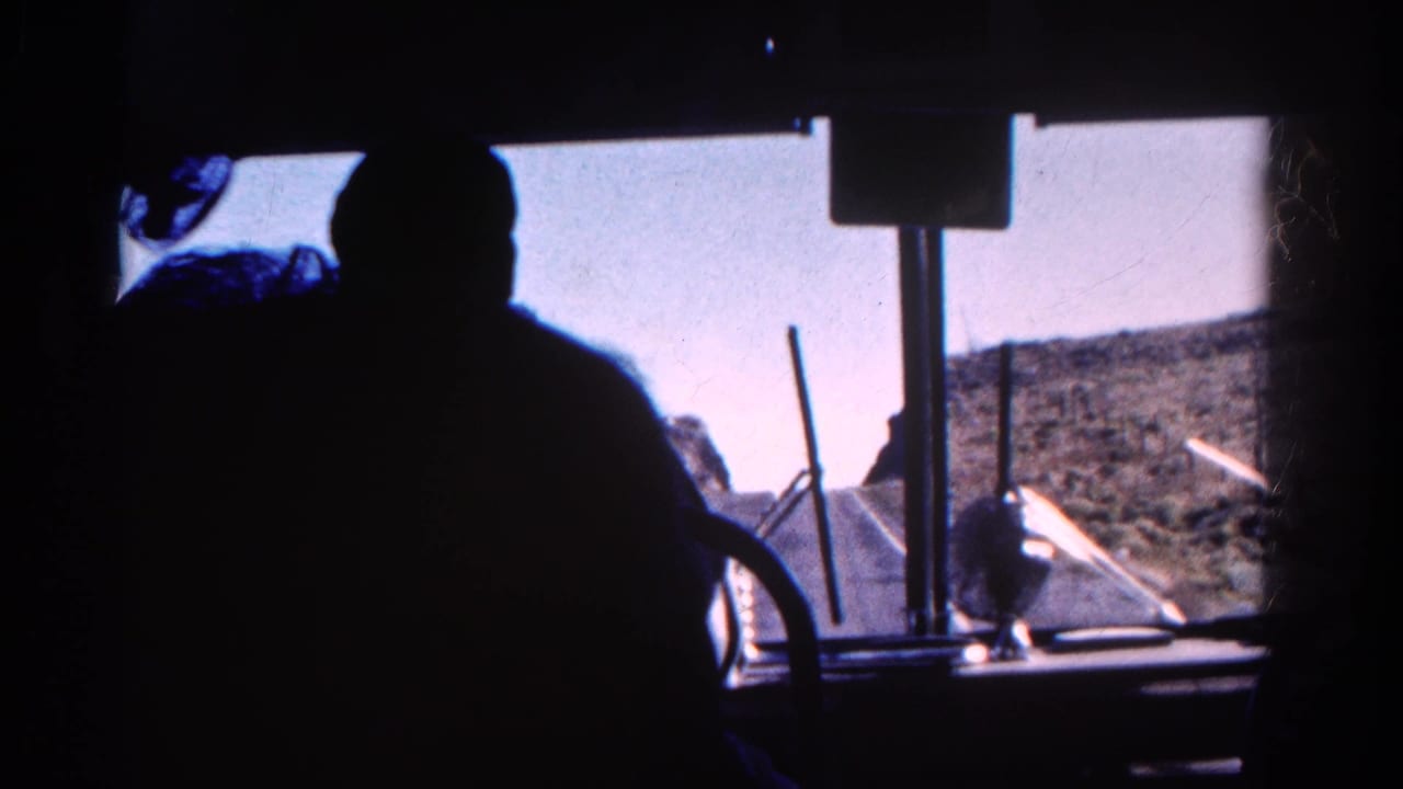 1967 Colorado 8mm frame from inside a train cab, with a silhouetted figure, windshield hardware, bright sky, and rocky mountain slope ahead.
