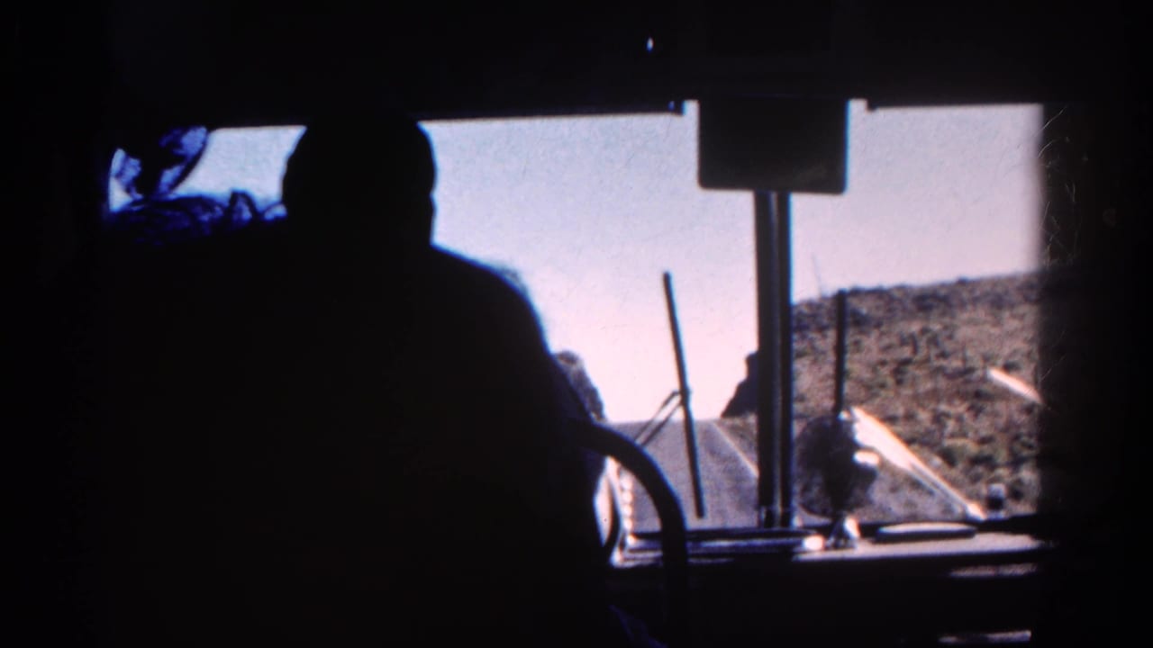 Dark figure in a train cab seen against a bright windshield and sloping mountain terrain.