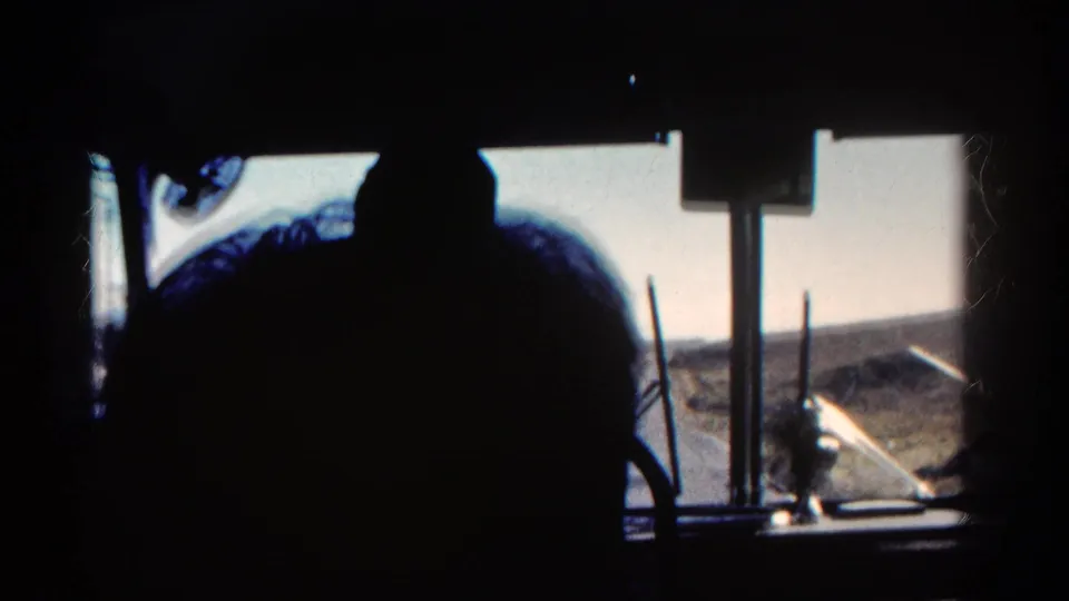 Interior bus view in Colorado, 1967, with a dark passenger profile against bright windows and dry rolling terrain outside.