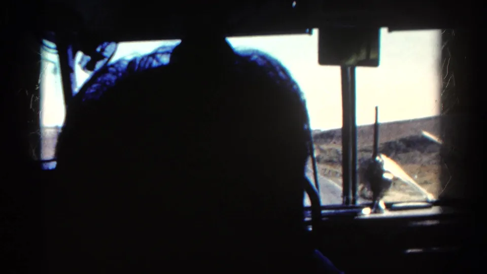 1967 bus passenger view in Colorado, showing a silhouetted person, window posts, and sunlit arid terrain outside.
