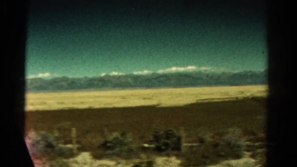 Colorado landscape view from the bus, with scrubby desert ground, distant mountains, and a clear blue-green sky on 8mm film.