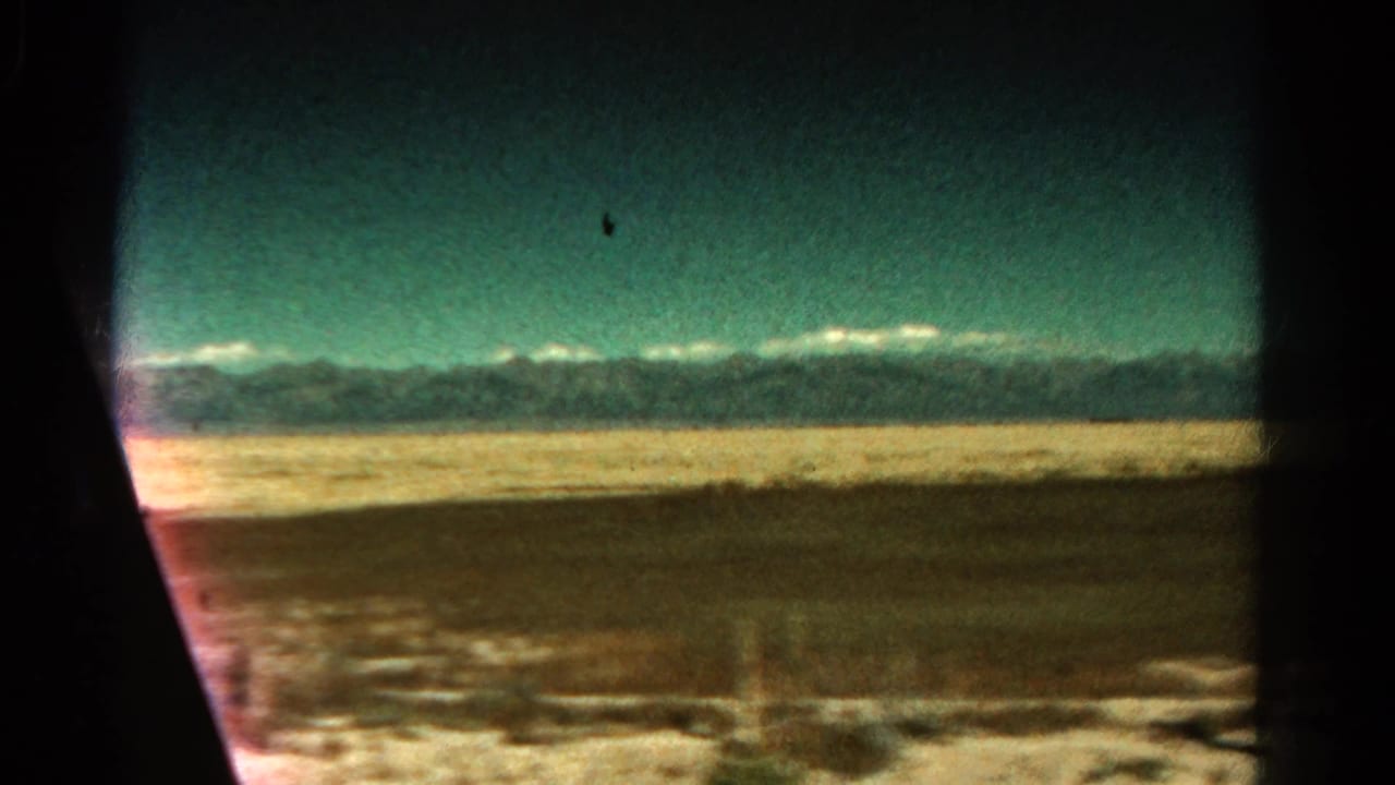 Colorado passenger-train window view showing open lowland, a pale horizon band, and mountains under a teal-tinted sky.