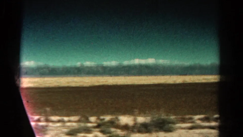 1967 Colorado road-view frame with snow-capped mountains beyond an open plain, seen through the edge of a moving vehicle window.