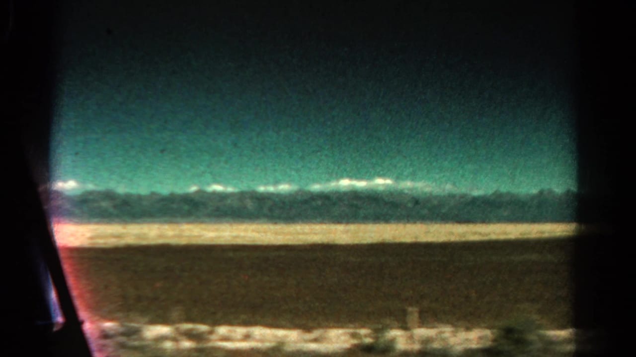 Open plain and distant mountain range framed by dark edges of a vehicle window.