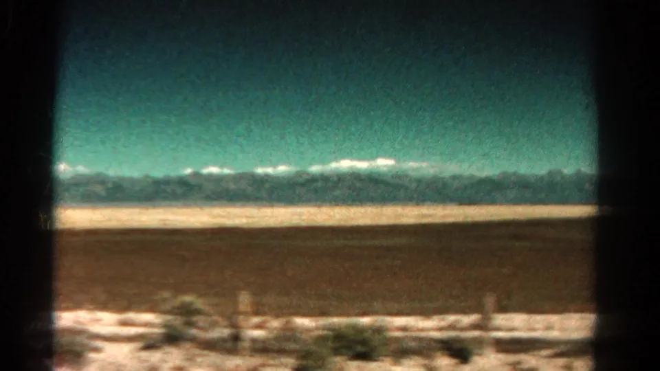 1967 Colorado home-movie view of roadside snow, open terrain, and a distant snow-capped range filmed from a moving car.