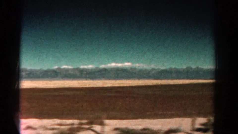 Final 1967 Colorado road-view frame showing a broad plain, distant snowy mountains, and the dark edge of a vehicle window.