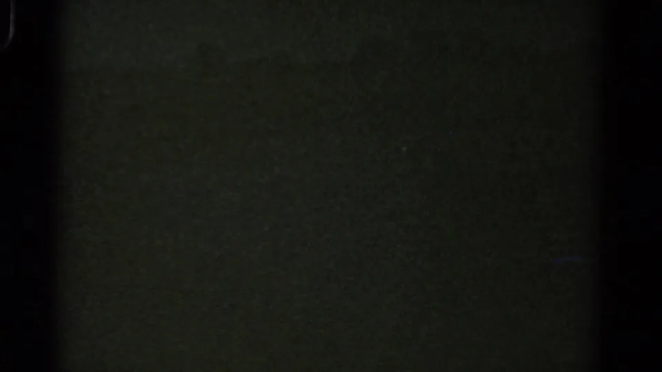 Underexposed 1967 8mm Colorado frame showing mostly darkness, greenish film texture, grain and gate-edge shadowing.