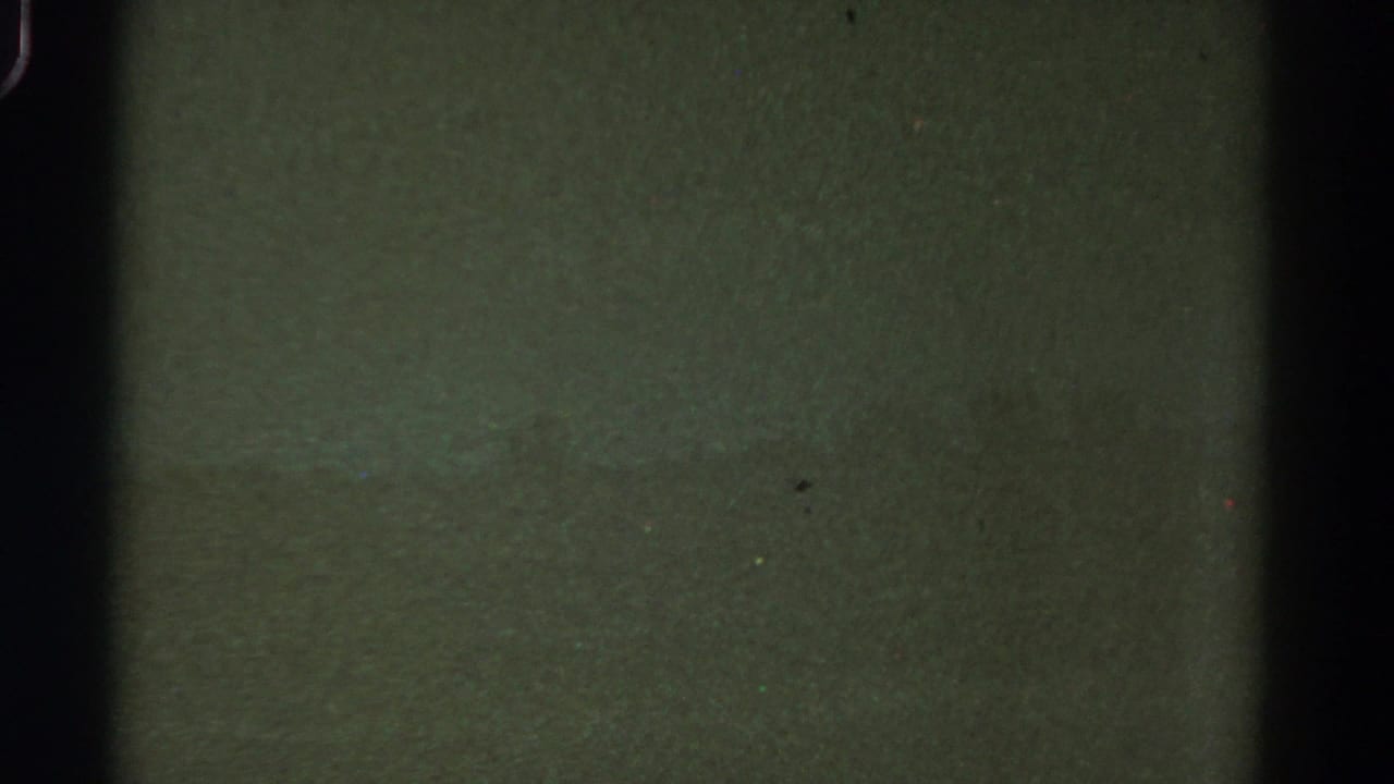 1967 Colorado 8mm frame with indistinct green landscape tones, heavy grain, dust specks, and dark film-edge shadows.