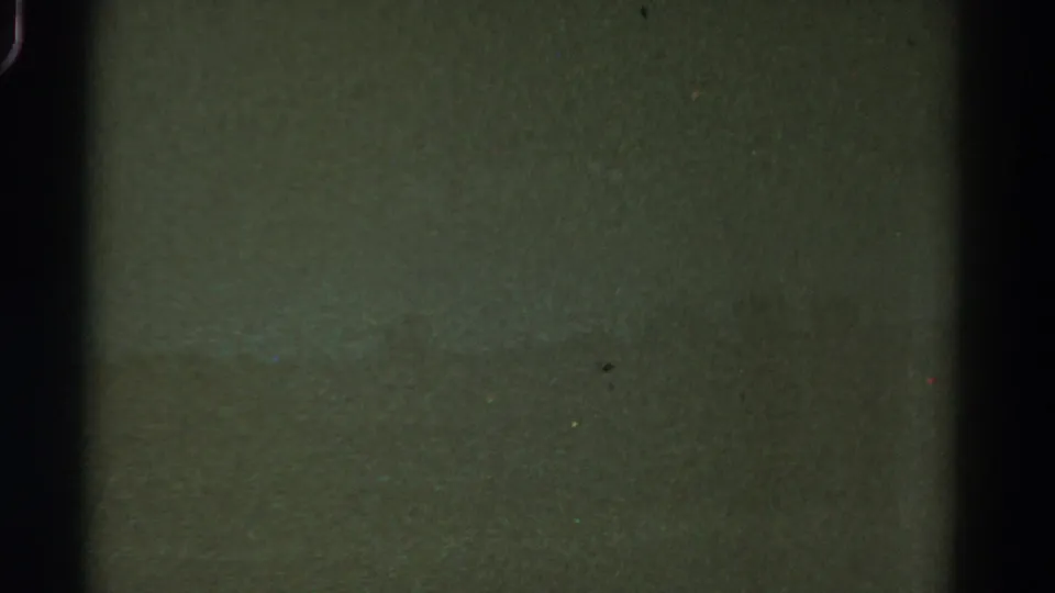 1967 Colorado 8mm frame with indistinct green landscape tones, heavy grain, dust specks, and dark film-edge shadows.
