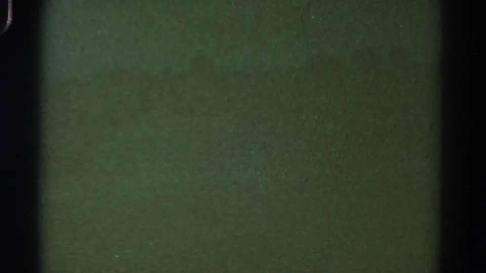 1967 Colorado 8mm frame with greenish low-contrast texture, central dark film-edge shadow, grain, and small dust specks.