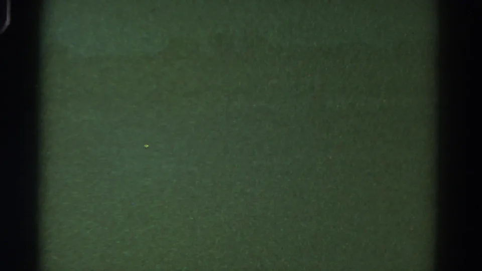 1967 Colorado 8mm frame with indistinct green landscape texture, heavy grain, scattered dust, and dark film-edge shading.