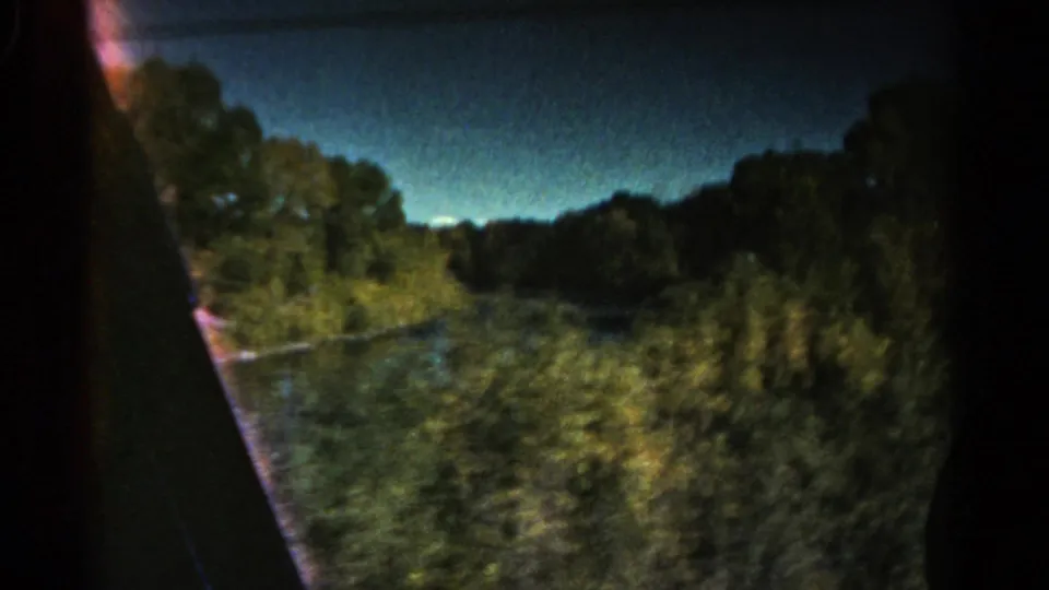 1967 Colorado 8mm frame with roadside trees, water, a dark frame edge, and motion blur from a moving vehicle.