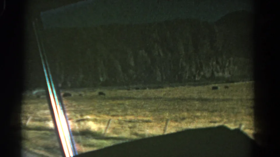 1967 Colorado 8mm frame with the vehicle interior silhouetted against dry fields, distant hills, a roadside sign, and the road edge.