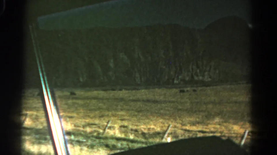 1967 Colorado home-movie frame looking through the car window at dry roadside grass, fence posts, low hills, and dark interior framing.