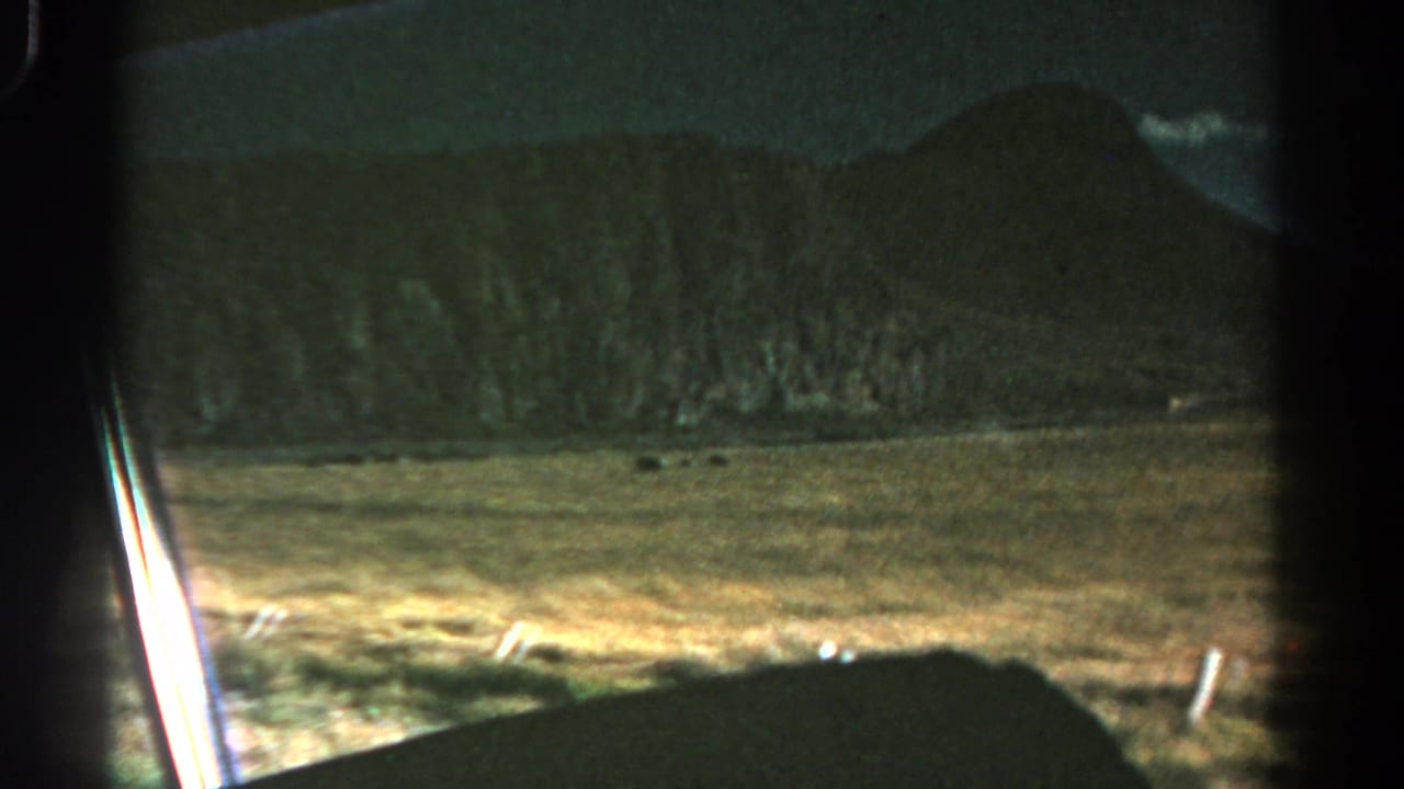 A moving 8mm view across Colorado fields toward low mountains, with window framing visible at the edge.