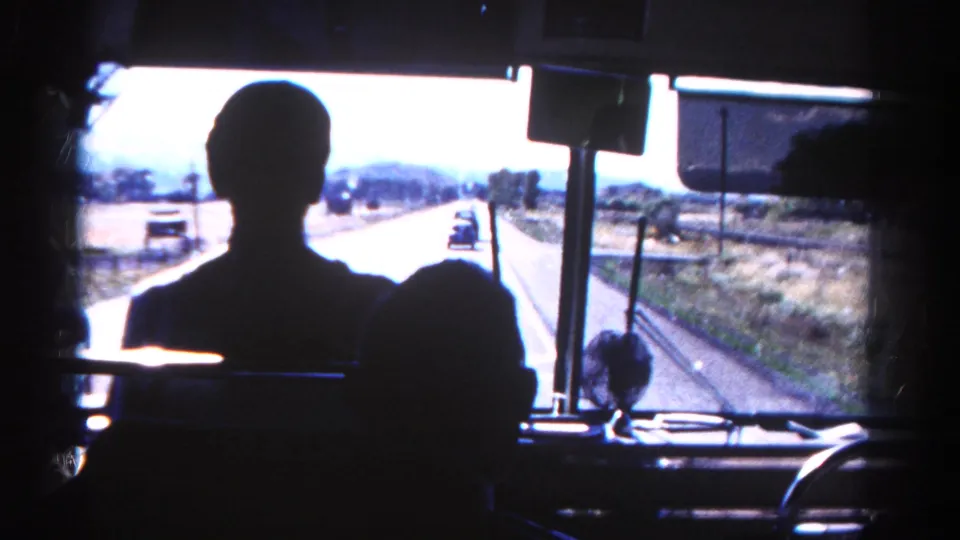 Inside a Colorado tour bus, silhouetted passengers face the windshield as cars travel on the sunlit road ahead.