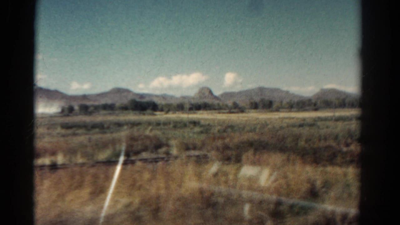 1967 Colorado 8mm frame showing dry grassland and distant mountains through a train window, with glass reflections in the foreground.