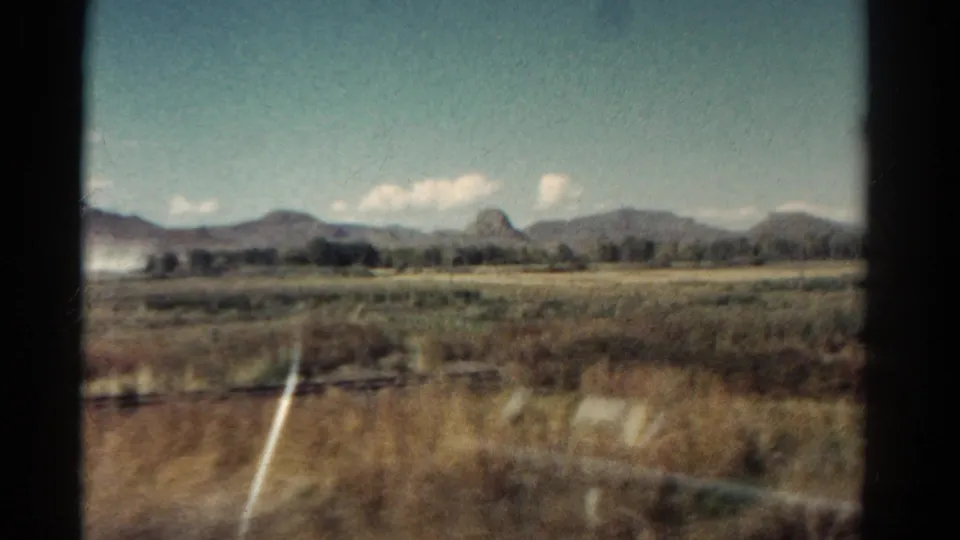 1967 Colorado 8mm frame showing dry grassland and distant mountains through a train window, with glass reflections in the foreground.