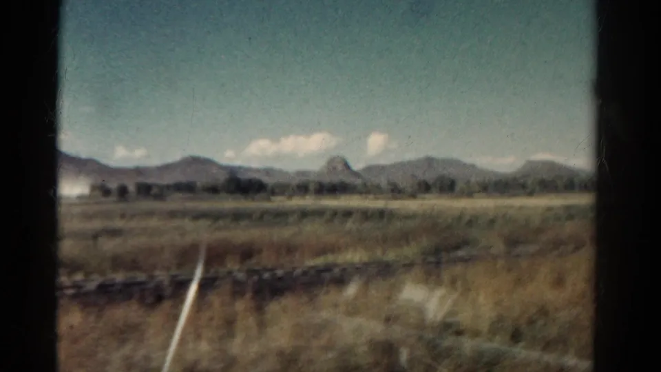 1967 Colorado rail-travel view with plains, distant mountains, a dark window edge, and a white trackside marker passing near the glass.