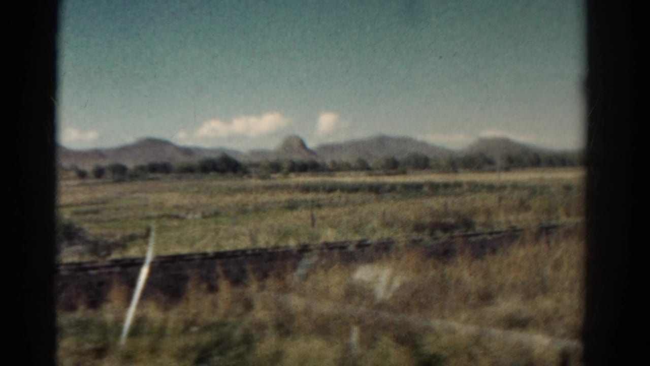 1967 Colorado 8mm view from a moving train, showing open grassland, fence lines, distant mountains, and scattered clouds.