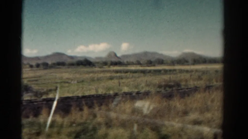 1967 Colorado 8mm view from a moving train, showing open grassland, fence lines, distant mountains, and scattered clouds.
