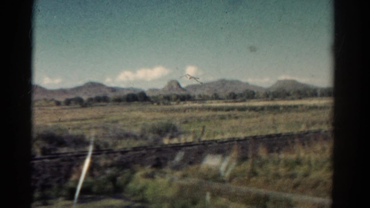 Rural field and mountain ridge framed by dark train-window edges.