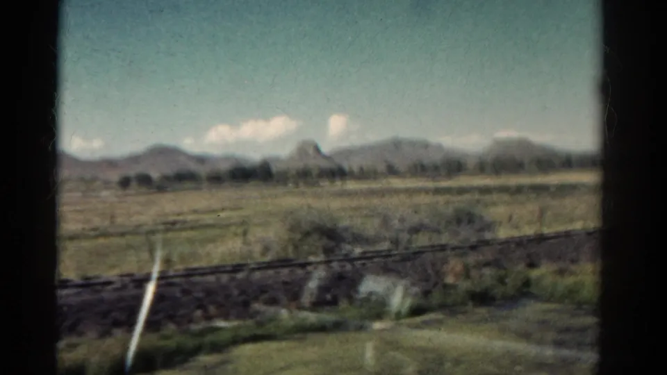 1967 Colorado countryside seen from a moving train, with pasture, fence lines, low mountains, and film gate edges visible.