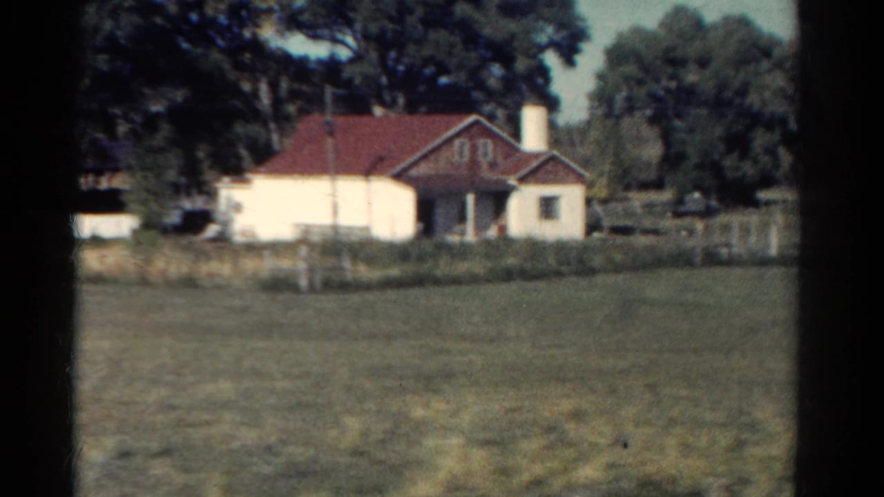 Red-roofed house across an open field with trees behind it.