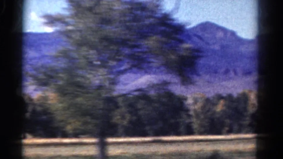 Motion-blurred roadside vegetation crosses a 1967 Colorado mountain view filmed from inside or beside a moving car.