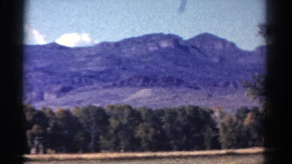 Colorado mountain ridge, dark forest edge and open field appear in a soft 1967 8mm road-trip frame.