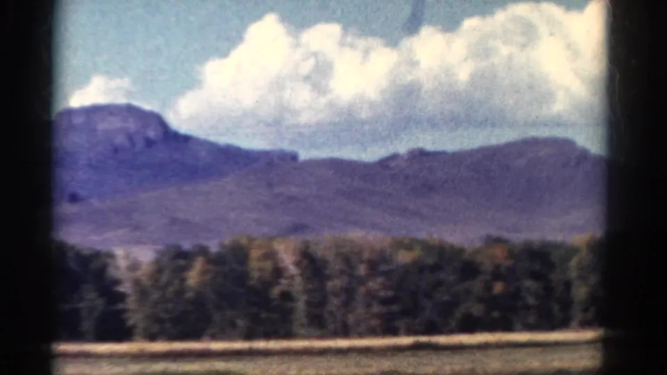 1967 Colorado 8mm landscape with large white clouds, distant mountains, forest, and dry foreground grasses.