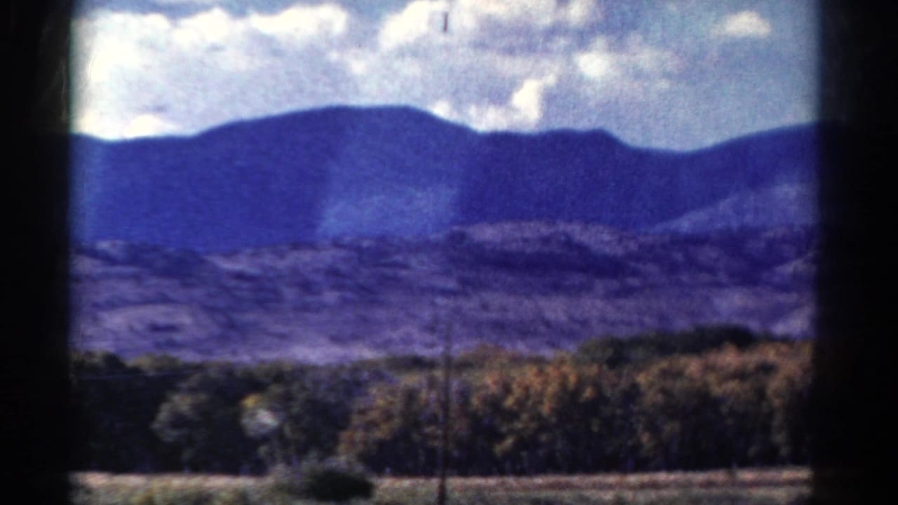 Distant mountains behind trees and fields under cloudy sky.