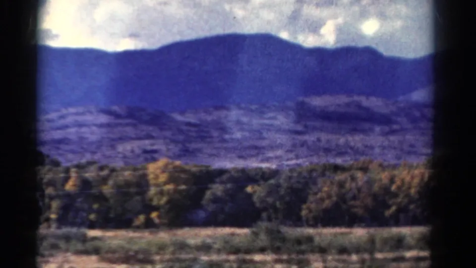 1967 Colorado countryside frame showing fields, autumn trees, and distant blue mountains through 8mm film borders.