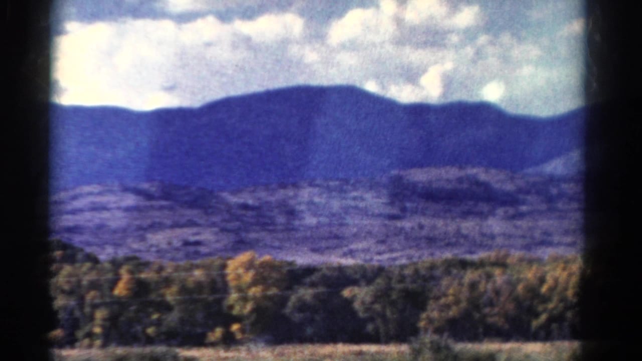 1967 Colorado 8mm view of a blue mountain ridge beyond trees and open land, framed by dark window or film edges.