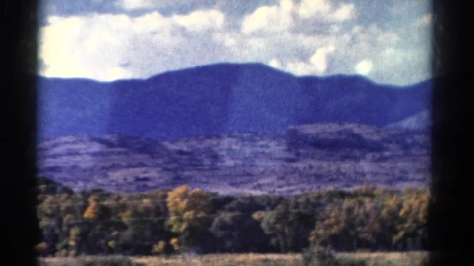 1967 Colorado 8mm view of a blue mountain ridge beyond trees and open land, framed by dark window or film edges.