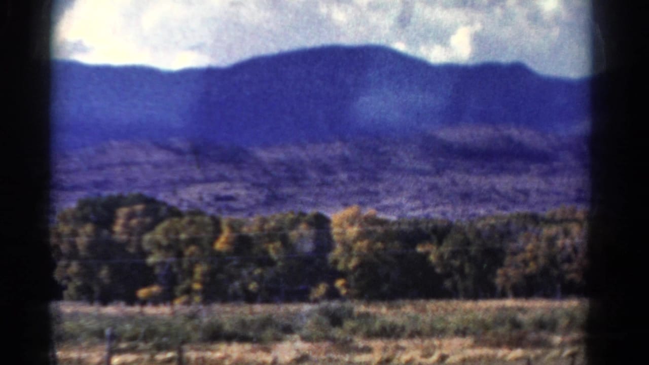 Blue mountain ridge, cloudy sky, tree line, and field in a soft moving view.